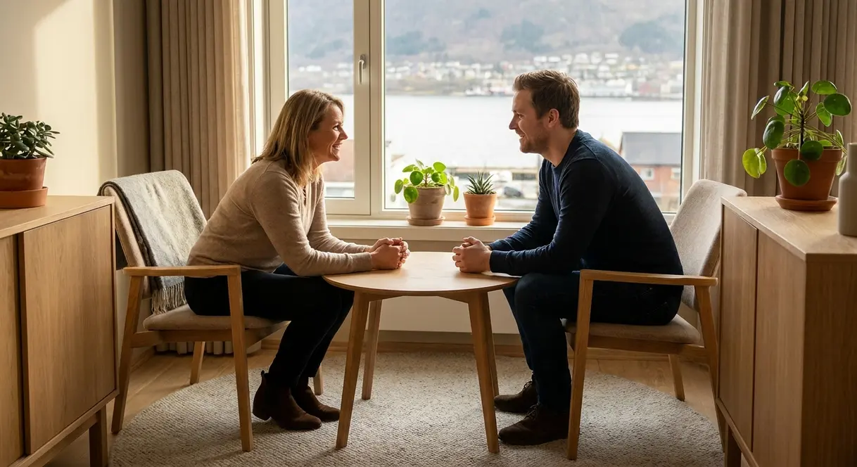 En leder sitter i en rolig og trygg samtale med en medarbeider på et kontor, begge lener seg frem i engasjert dialog.